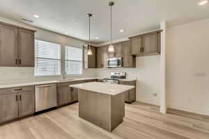 Kitchen with decorative light fixtures, stainless steel appliances, a kitchen island, and light hardwood / wood-style floors