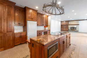 Kitchen with stainless steel microwave, black electric stovetop, white refrigerator, decorative backsplash, and a kitchen island