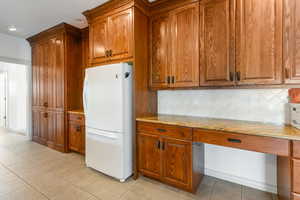 Kitchen with light tile patterned floors, white refrigerator, tasteful backsplash, and built in desk