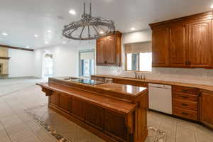 Kitchen featuring backsplash, white dishwasher, black electric cooktop, light tile patterned floors, and a kitchen island