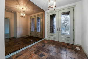 Entrance foyer with an inviting chandelier, stone finish floor, french doors, and baseboards