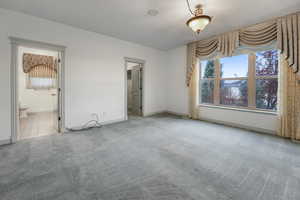 Unfurnished bedroom featuring ensuite bathroom, a textured ceiling, carpet, and baseboards