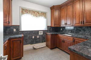 Kitchen with backsplash, dark stone countertops, sink, and light tile patterned flooring