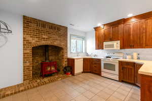 Basement Kitchen with white appliances, backsplash, a wood stove, sink, and light tile patterned floors