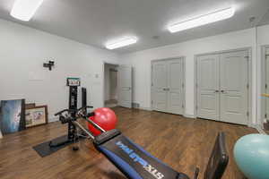 Workout area featuring a textured ceiling, visible vents, wood finished floors, and baseboards