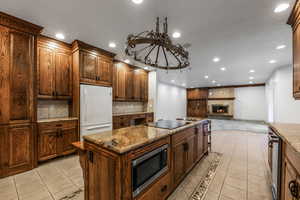 Kitchen featuring stainless steel microwave, black electric cooktop, light tile patterned floors, and freestanding refrigerator