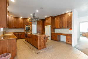 Kitchen with white refrigerator, sink, hanging light fixtures, light tile patterned floors, and a kitchen island