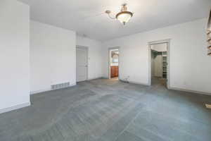 Unfurnished bedroom with light colored carpet, visible vents, baseboards, ensuite bath, and a walk in closet