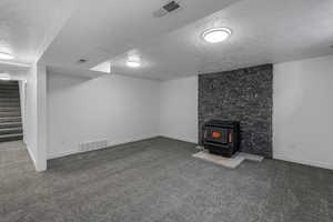 Basement featuring dark carpet, a textured ceiling, and a wood stove