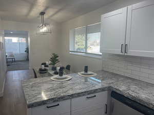 Kitchen with dark hardwood / wood-style flooring, backsplash, stainless steel dishwasher, pendant lighting, and white cabinets