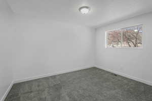 Empty room featuring dark colored carpet and a textured ceiling