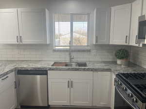 Kitchen with white cabinets, decorative backsplash, sink, and appliances with stainless steel finishes