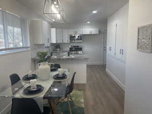 Kitchen with decorative backsplash, stainless steel appliances, dark wood-type flooring, pendant lighting, and white cabinetry