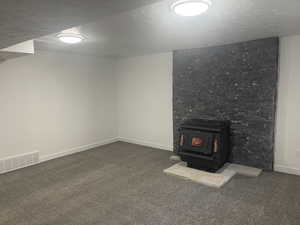 Basement with carpet flooring, a wood stove, and a textured ceiling