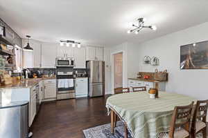 Kitchen featuring hanging light fixtures, white cabinets, stainless steel appliances, and sink