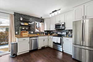 Kitchen featuring dark stone countertops, white cabinetry, dark hardwood / wood-style flooring, and stainless steel appliances