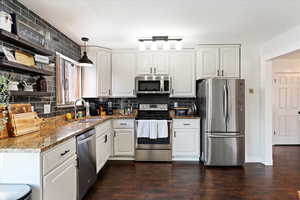 Kitchen with white cabinetry, sink, stainless steel appliances, dark hardwood / wood-style floors, and pendant lighting