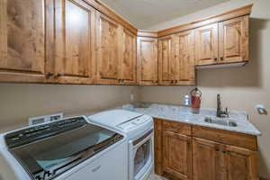 Laundry room with cabinets, a textured ceiling, washing machine and clothes dryer, and sink