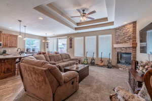 Living room featuring ceiling fan with notable chandelier, light hardwood / wood-style floors, a stone fireplace, and a textured ceiling