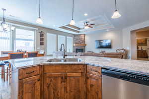 Kitchen with dishwasher, a raised ceiling, sink, a fireplace, and light stone counters