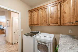 Laundry area with light hardwood / wood-style flooring, cabinets, a textured ceiling, and independent washer and dryer