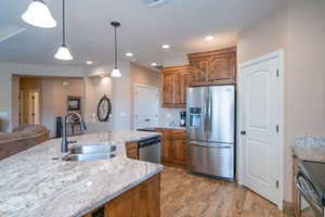 Kitchen featuring light stone countertops, sink, light hardwood / wood-style flooring, pendant lighting, and appliances with stainless steel finishes