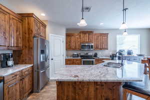 Kitchen featuring appliances with stainless steel finishes, a center island with sink, decorative light fixtures, and sink