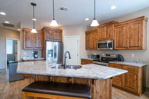 Kitchen with stainless steel appliances, a kitchen island with sink, sink, decorative light fixtures, and light hardwood / wood-style floors