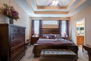 Bedroom with a tray ceiling, ensuite bathroom, ceiling fan, and light carpet