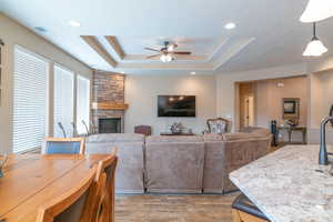 Living room featuring ceiling fan, a raised ceiling, a fireplace, and light hardwood / wood-style flooring