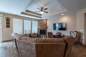 Living room featuring a raised ceiling, hardwood / wood-style flooring, ceiling fan, a fireplace, and a textured ceiling