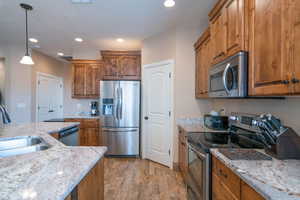 Kitchen featuring light stone countertops, stainless steel appliances, sink, pendant lighting, and light hardwood / wood-style flooring