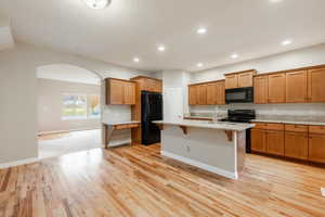 Kitchen featuring sink, a kitchen bar, a kitchen island with sink, black appliances, and light wood-type flooring