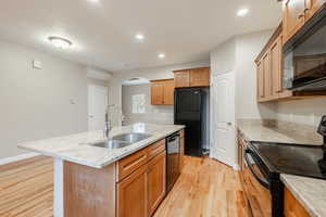 Kitchen with light stone countertops, sink, black appliances, light hardwood / wood-style floors, and an island with sink