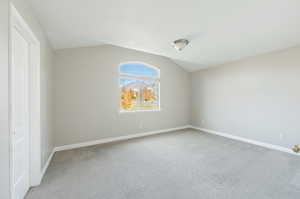 Empty room featuring carpet and vaulted ceiling