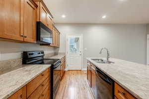 Kitchen with light stone counters, light hardwood / wood-style flooring, black appliances, and sink