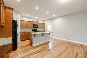 Kitchen featuring light wood-type flooring, a textured ceiling, black appliances, a center island with sink, and a breakfast bar area