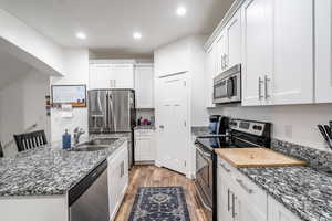 Kitchen with dark stone countertops, light hardwood / wood-style flooring, white cabinets, and appliances with stainless steel finishes