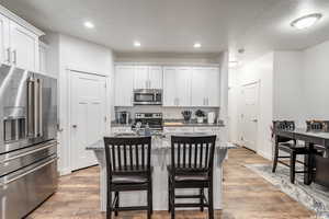 Kitchen with white cabinets, appliances with stainless steel finishes, light stone counters, and a kitchen island with sink