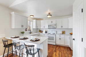 Kitchen with white cabinets, white appliances, kitchen peninsula, and a breakfast bar area