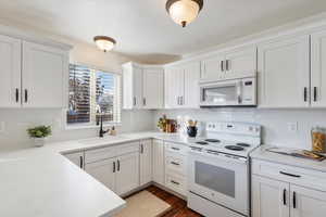 Kitchen with white appliances, backsplash, sink, dark hardwood / wood-style flooring, and white cabinetry