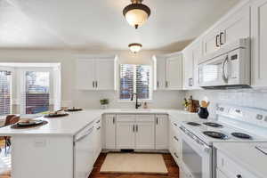 Kitchen featuring kitchen peninsula, white appliances, white cabinetry, and a wealth of natural light