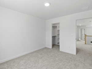 Unfurnished bedroom with a spacious closet, light carpet, and a closet