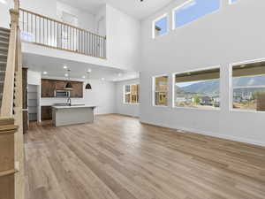 Unfurnished living room with a mountain view, a healthy amount of sunlight, a high ceiling, and light wood-type flooring