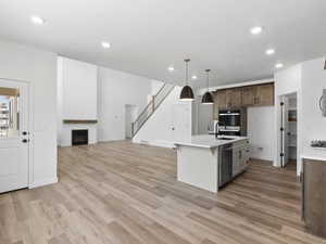 Kitchen featuring light wood-type flooring, stainless steel dishwasher, sink, decorative light fixtures, and an island with sink