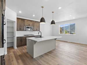 Kitchen with gas cooktop, light wood-type flooring, a kitchen island with sink, sink, and pendant lighting