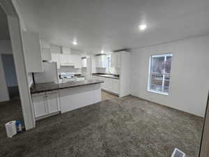 Kitchen with white cabinets, white appliances, kitchen peninsula, and sink