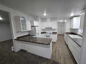 Kitchen with white appliances, dark wood-type flooring, sink, white cabinetry, and kitchen peninsula