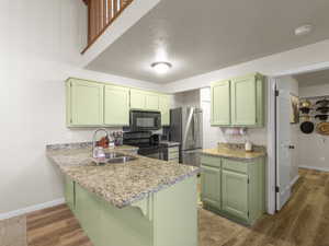 Kitchen featuring kitchen peninsula, sink, black appliances, and green cabinetry