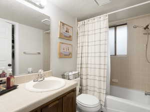 Full bathroom with shower / bath combo with shower curtain, vanity, a textured ceiling, and toilet